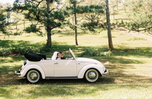 un matrimonio conduciendo un coche de boda clásico en un pinar