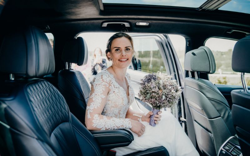 una novia sonriente sentada en el interior de un coche para bodas